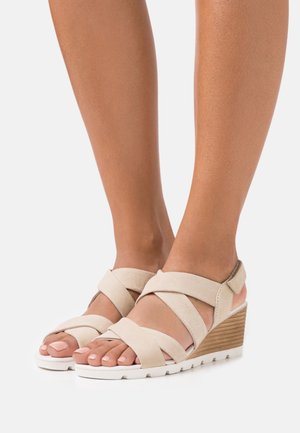 Sandalias de cuña beige con tiras de ante entrelazadas, una plantilla de madera texturizada y una suela de goma blanca. Diseño de punta abierta.