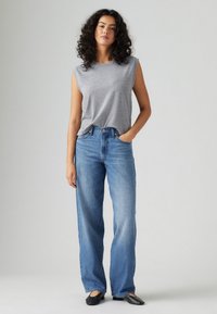 Sivi majica bez rukava, svijetlo plave traperice širokih nogavica, crne baletanke. Glatka tekstura, ležeran dizajn, s opuštenim krojem i visokim pojasom.