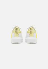 Valged sneakers metallik kuldsete aktsentidega kontsapidudel, kollase logo detailidega ja tekstuurse naha mustriga. Paksud valged kummitaldad.