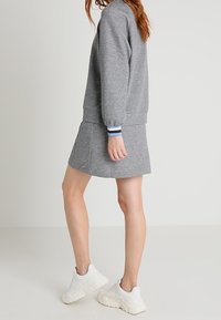 Sudadera gris combinada con una minifalda gris. La sudadera tiene puños acanalados con rayas azul y blanca. Se lleva con zapatillas blancas.