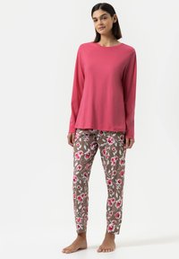 Roze lange mouwen shirt met een ronde hals, gecombineerd met bruin gebloemde broek met roze en witte bloemen. Gladde stof structuur.