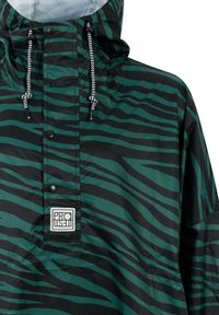 Zielono-czarna kurtka przeciwwiatrowa w paski zebry z kapturem, z zapięciem na zatrzaski z przodu i fakturowanym wykończeniem. Haftowana naszywka na klatce piersiowej.
