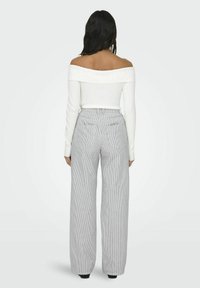 Vit off-shoulder ribbad topp i kombination med högmidjade byxor med vida ben, som har ett vertikalt randigt mönster i grått och vitt.