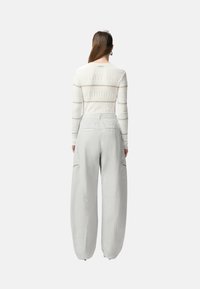 Top bianco a maniche lunghe con righe beige, abbinato a pantaloni cargo grigi chiari dal fit ampio con tasche con zip.