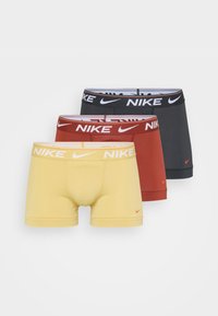 Drie paar Nike boxershorts in geel, rood en donkergrijs. Elk heeft een opvallende tailleband met het merklogo duidelijk weergegeven.