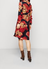 Abito floreale con sfondo blu navy, caratterizzato da grandi fiori rossi e gialli, maniche lunghe e vita cintrata. Stivali alla caviglia con tacco marroni.