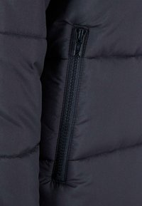 Chaqueta acolchada negra con una cremallera visible. La tela es suave, presenta un diseño acolchado y un acabado mate.