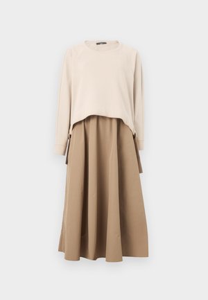 Haut beige à manches longues et col rond superposé à une jupe midi évasée taille haute couleur beige clair, sur fond blanc.