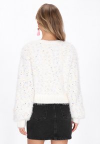 Valkoinen pörröinen neule, jossa on värikkäitä täpliä, ilmavat hihat ja ribattu helma. Yhdistetty mustaan farkkuhameeseen.