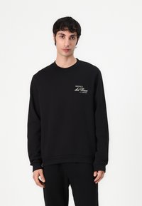 Czarny sweatshirt z miękkiego bawełnianego materiału, z długimi rękawami, okrągłym dekoltem i białym nadrukiem graficznym na lewej piersi.