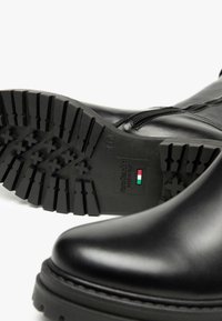 Schwarze Lederstiefeletten mit einem wasserdichten Reißverschluss, strukturiertem Gummiunterboden und eingeprägtem Markenzeichen. Sie verfügen über eine abgerundete Zehenform und eine dicke Sohle.