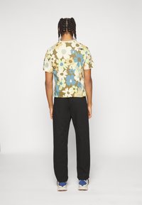 Koszulka z krótkim rękawem w beżowy, niebieski i zielony wzór kwiatowy; połączona z czarnymi spodniami; osoba tyłem, w niebiesko akcentowanych butach sportowych.