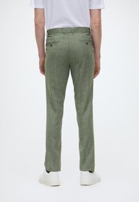 Figurbetonte, grüne, strukturierte Hose mit einem subtilen Muster, ausgestattet mit zwei Gesäßtaschen und einem normalen Bund, kombiniert mit weißen Sneakers.