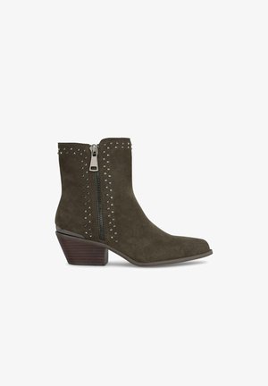 Bottines en daim vert olive avec fermeture éclair sur le côté, ornées de clous en argent le long de la ligne de fermeture éclair et d'un talon empilé pour un peu plus de hauteur.