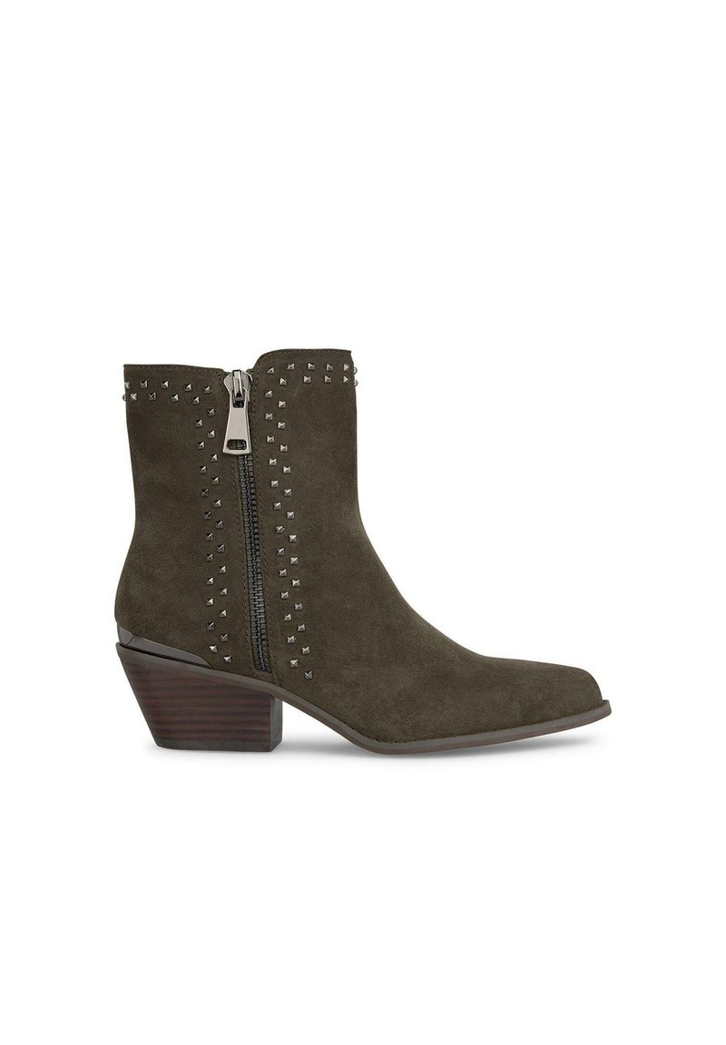 Botas de ante verde oliva hasta el tobillo con cremallera lateral, adornadas con tachuelas plateadas a lo largo de la línea de la cremallera y un tacón apilado para mayor altura.