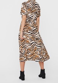 Sukienka midi w print zwierzęcy z krótkimi rękawami, z falistym wzorem w pomarańczowym i czarnym, wykonana z lekkiego materiału, zestawiona z czarnymi botkami za kostkę.