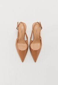 Chaussures slingback à bout pointu en cuir verni beige brillant. Elles présentent un talon fin, une bride à la cheville avec boucle, et une doublure intérieure lisse.