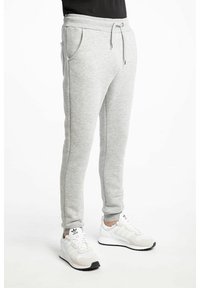 Pantalons de survêtement gris avec une taille à cordon, poches latérales et jambes fuselées, associés à des chaussures de sport blanches avec des accents noirs.