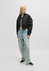 Svart kort bomberjacka med en ficka på ärmen, tillsammans med bleka oversized denimjeans och svarta platåskor.