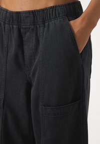 Svart denimbukser med elastisk midje, sidelommer og avslappet passform. Stoffet har en subtil tekstur og solid søm.