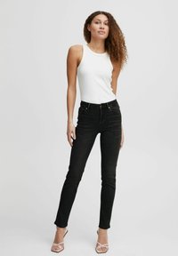 Jeans negros ajustados con cintura alta, combinados con una blusa sin mangas blanca y sandalias blancas de tiras. Tejido suave con un detailing mínimo.