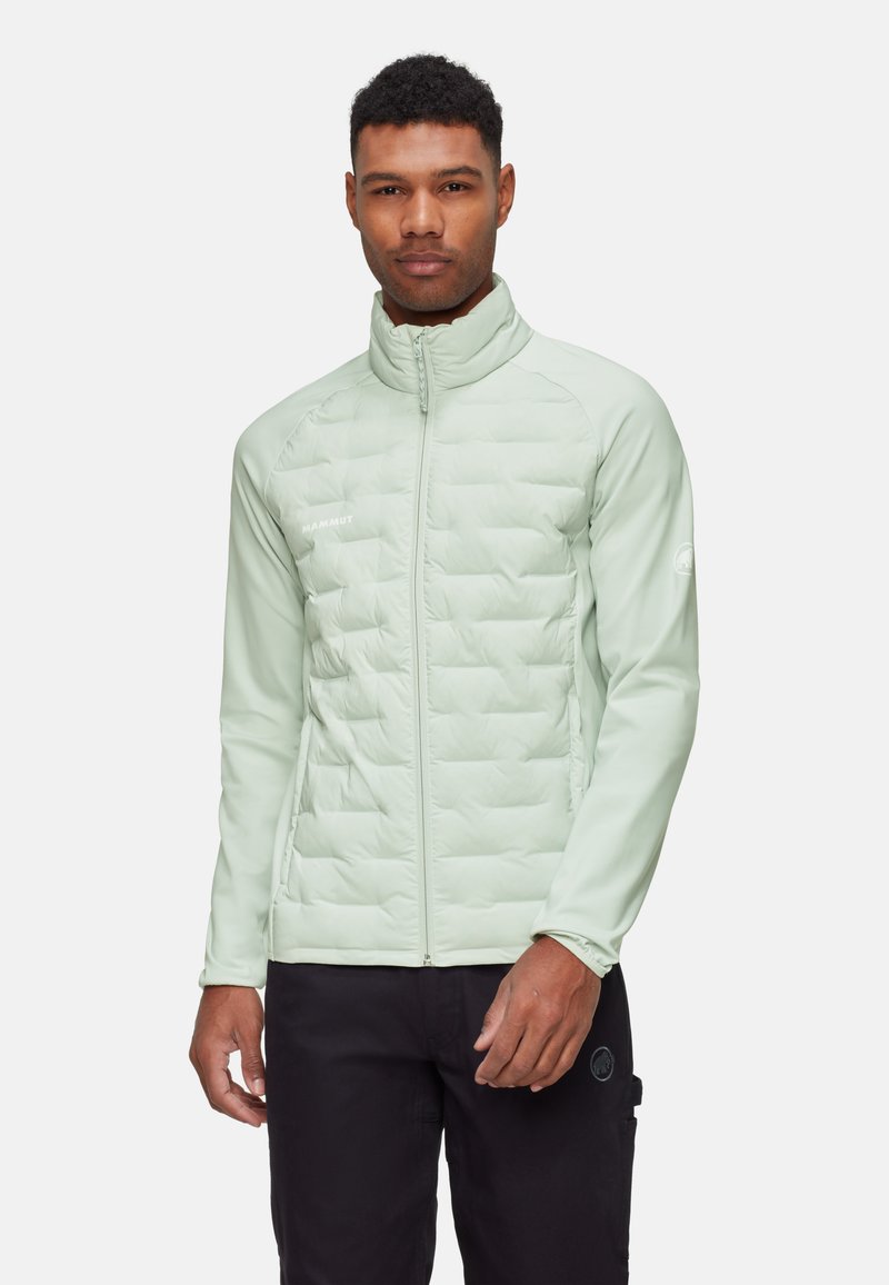 Jasnozielona, ocieplana kurtka z pikowanym wzorem, wysoki kołnierz, pełny zamek błyskawiczny i elastyczne mankiety. Noszona z czarnymi spodniami.