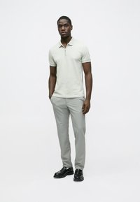 Gaiši pelēka polo krekls ar rāvējslēdzēja aizdari, kopā ar gaiši pelēkām biksēm un melniem apaviem. Vienkāršs dizains ar tīru, gludu tekstūru.