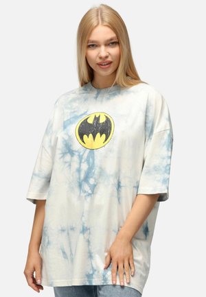 Camiseta de gran tamaño, de color claro, con diseño de tie-dye y un logo de Batman en negro y amarillo en el pecho. Material de algodón, con mangas cortas y diseño de cuello redondo.