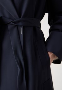 Bata de color azul marino hecha de tela suave, con cintura ajustable, bolsillos ocultos y una textura sutil con un acento plateado brillante.