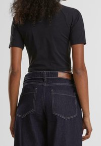 Svart kortärmad topp i kombination med mörka denimjeans med en läderpatch bak, synlig söm och sidofickor.