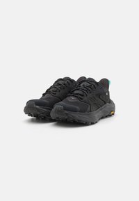 Pantofi sport negri cu un superior din plasă, detalii texturate și o talpă robustă. Caracteristicile includ un design cu șireturi și un accent verde vibrant la călcâi.