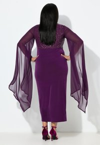 Fialové šaty s flitrovaným živůtkem a průsvitnými, proudivými rukávy. Přiléhavý střih sahá do poloviny lýtek. Doplněné o živé, vysoké podpatky.