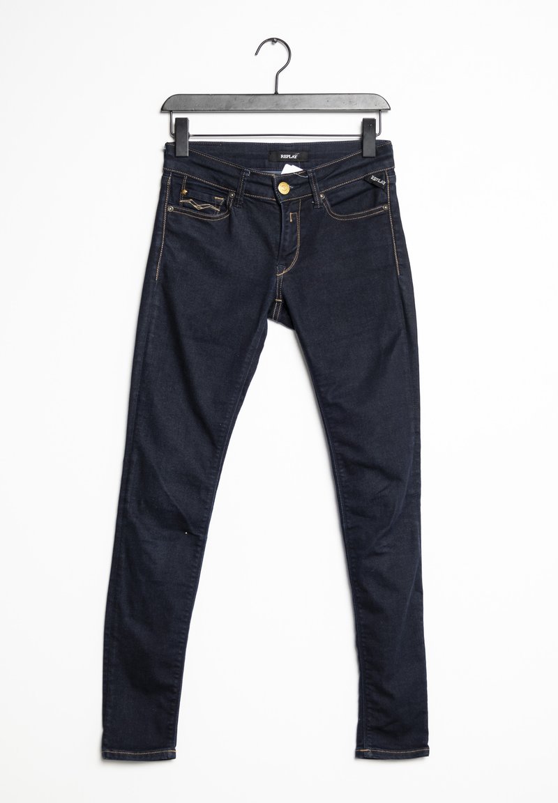 Jean skinny bleu foncé suspendu à un cintre noir sur un fond blanc.