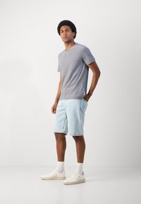 Gestreept grijze T-shirt met korte mouwen, gecombineerd met lichtblauwe denim shorts. Witte sneakers en enkelsokken maken de casual look compleet.