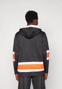 Juoda striukė su gobtuvu, turinti oranžines ir baltas juostas ant rankovių bei apatinio krašto. Pagaminta iš lygaus audinio su minkštu tekstūruotu gobtuvu.