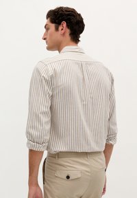 Camicia a righe in beige e bianco, realizzata in tessuto leggero. Presenta maniche arrotolate, yoke posteriore e un leggero etichetta al colletto.