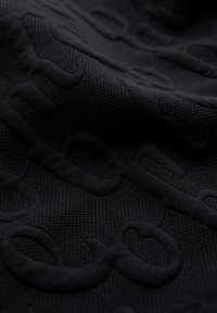 Tissu noir avec des lettres en relief et texturées créant un motif subtil et tactile sur la surface.