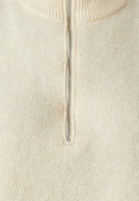 Cream-colored knit sweater with a high collar and a silver zippered front. Soft texture, lightweight, and subtle fuzzy detailing throughout.