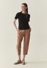 Haut noir à manches courtes associé à un pantalon ample couleur sable et des baskets marron. Tissu lisse avec un col rond classique et une silhouette décontractée.