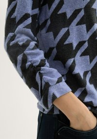 Blauer und schwarzer Hahnentritt-muster Fleece-Pullover mit rundem Ausschnitt und taillierten, umschlagbaren Ärmeln, kombiniert mit dunklen Denim-Jeans.