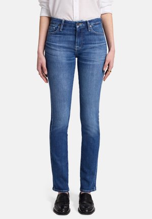 Jean en denim bleu moyen avec une coupe classique, un design à cinq poches et une légère décoloration, associés à des mocassins en cuir noir.