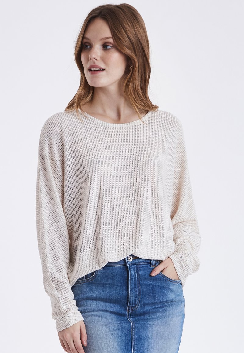 Hellbeige strukturierter Pullover mit lockerer Passform, langen Ärmeln und weitem Ausschnitt, kombiniert mit einem Jeansrock.