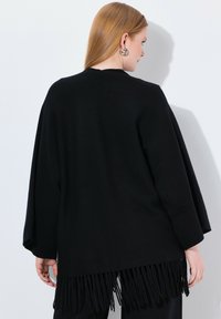 Schwarze Strickjacke mit lockerer Passform, mit fransigem Saum und langen Ärmeln. Glatte Textur und minimalistisches Design für vielseitigen Einsatz.