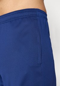 Lähedal kaader sinistest tekstureeritud spordilühikesed, millel on külgpocket ja elastne vöökoht, inimese taljel ja puusal.