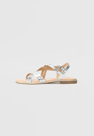 Silver flat sandals with multiple crossover straps, a textured metallic finish, and a minimalist design. Features a low, brown sole.