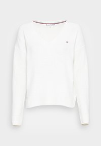 Witte gebreide trui met een V-hals, verlaagde schouders en geribde manchetten. Bevat een kleine logo-accent op de borst en een gestructureerde weving.