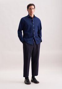 Camicia button-up blu navy con un tessuto texturizzato, abbinata a pantaloni scuri e scarpe stringate nere. La camicia presenta un colletto standard.