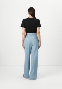 T-shirt noir à manches courtes associé à un jean en denim large et léger avec une taille haute et des coutures contrastantes.