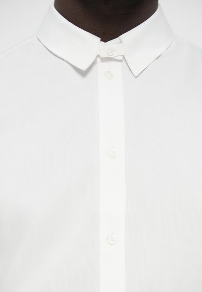 Chemise blanche à boutons, dotée d'un col classique, d'une texture lisse et de six boutons sur le devant, mettant en valeur un design épuré et minimaliste.