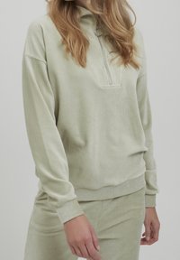 Pullover a mezzo zip in corduroy verde chiaro con maniche lunghe, dotato di tirazip a cerchio e polsini a coste, abbinato a pantaloni coordinati.